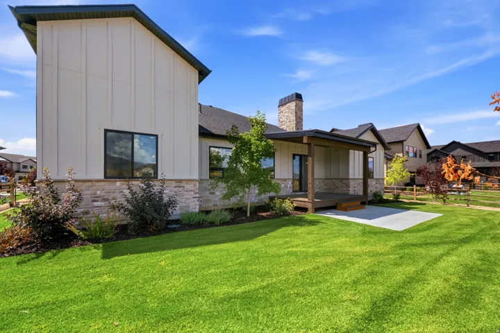 Expansive green lawn with a covered porch featuring wood decking and a concrete patio