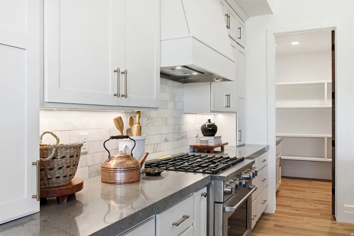 White shaker cabinetry, stone countertops, stainless steel range with hood, tile backsplash, and a walk-in pantry with shelving