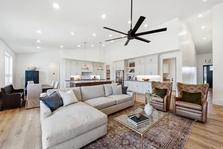 Open-concept living area featuring a vaulted ceiling with a contemporary ceiling fan, recessed lighting, wood-finish flooring, and a kitchen with white cabinetry and an island