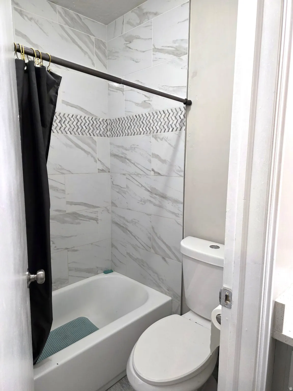 Bathtub with a shower, white tile surround, decorative mosaic tile accent, and a white toilet
