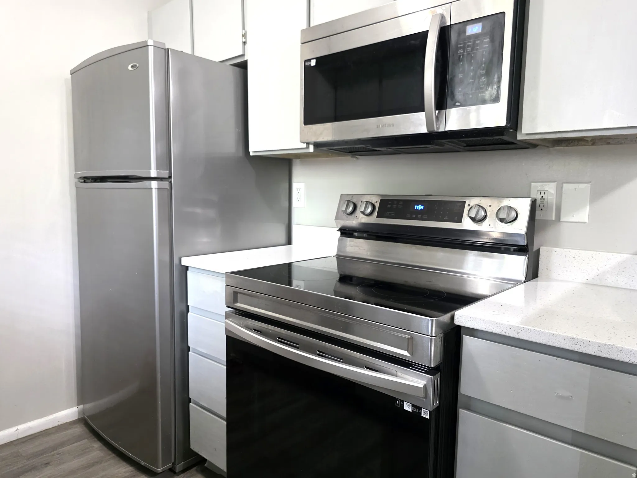 Stainless steel appliance suite, white upper cabinetry, light gray lower cabinetry, and light quartz countertops
