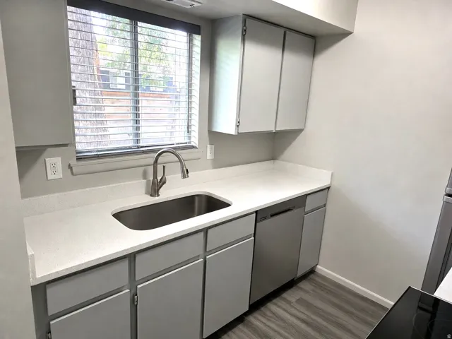 Compact kitchen featuring light gray cabinetry, light-toned countertops, a stainless steel sink with a gooseneck faucet, a stainless steel dishwasher, and wood-finish flooring