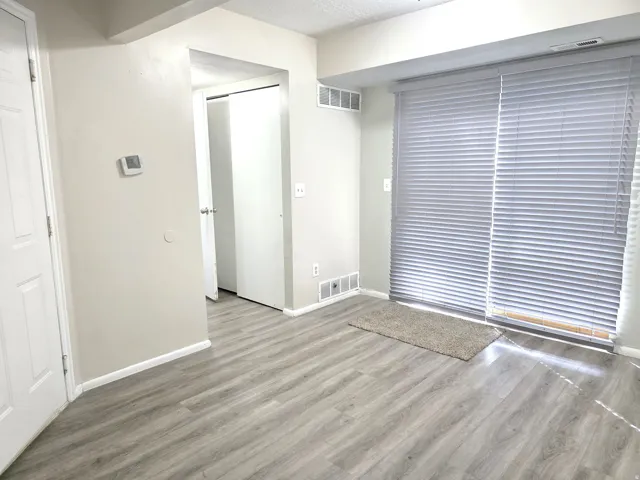 Wood-finish flooring throughout, sliding glass door with horizontal blinds, and a neutral wall palette