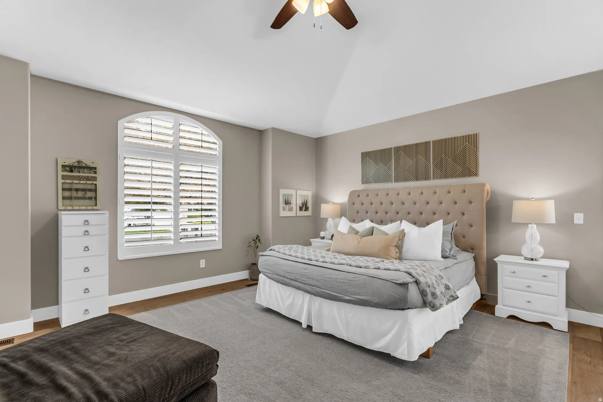 Vaulted ceiling with a ceiling fan, arched window with plantation shutters, wood-finish flooring, and wall-to-wall carpeting