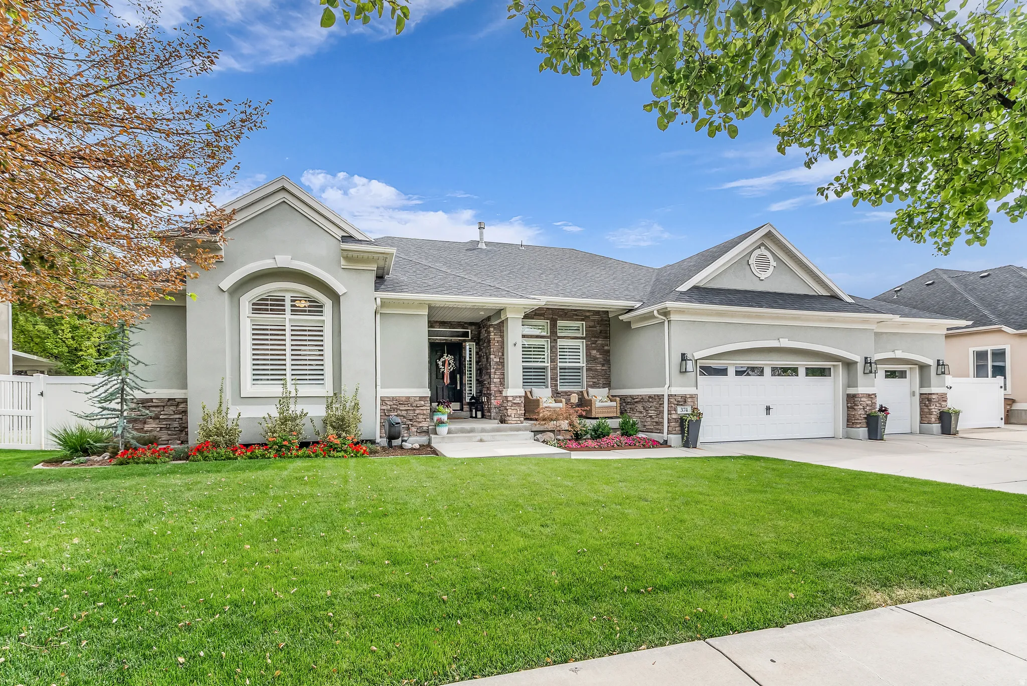 Stucco exterior with stone accents, a multi-car garage, established front landscaping, and a covered entry