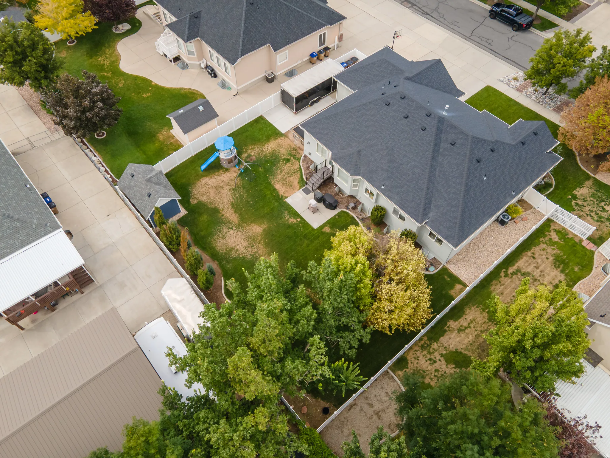 Expansive backyard featuring a patio, manicured lawn, white picket fencing, and mature trees