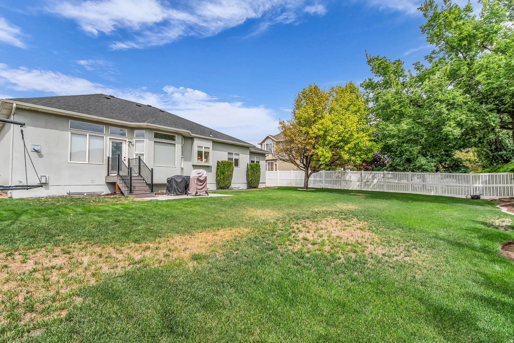 Expansive lawn with mature trees and a white privacy fence