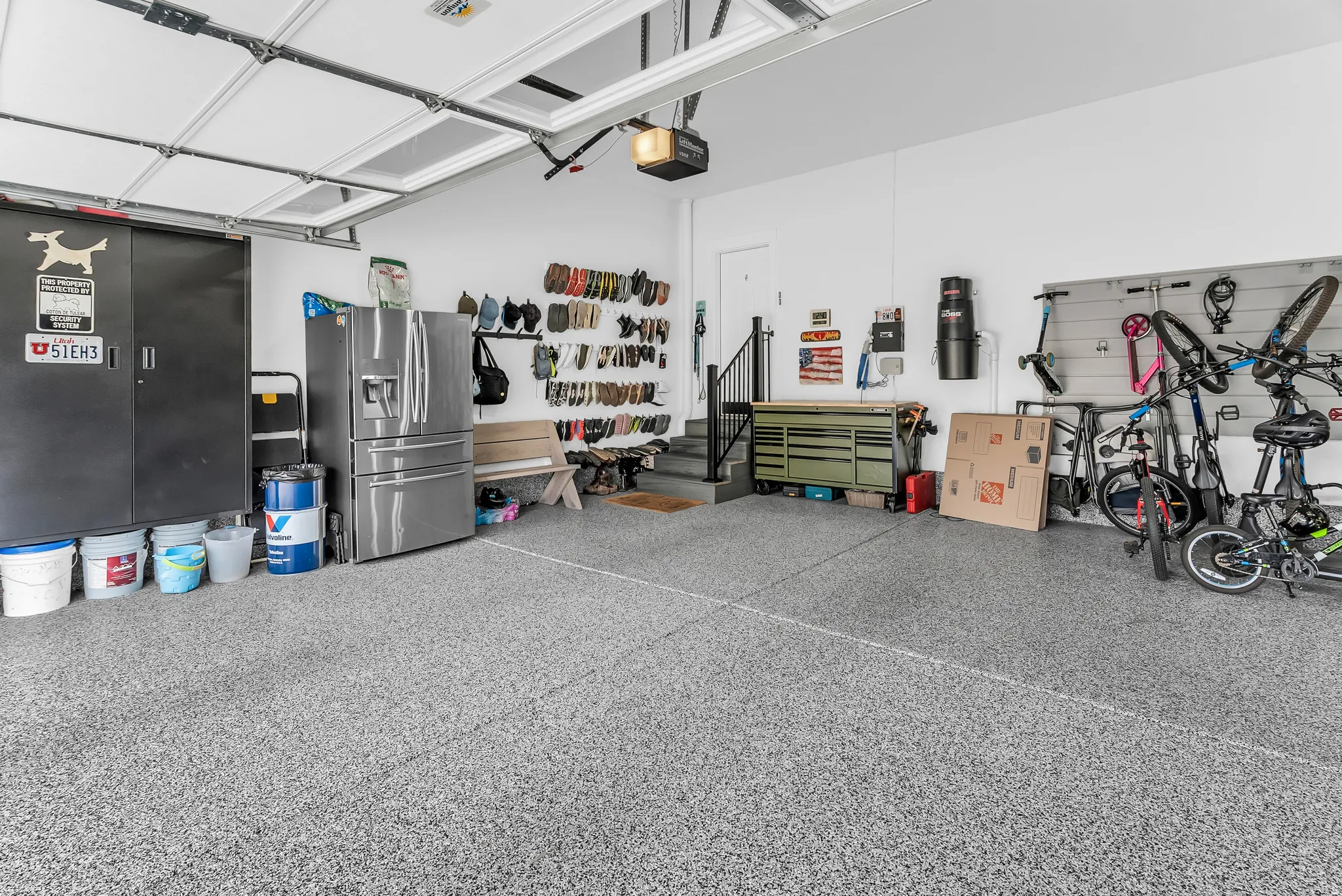 Garage featuring a textured concrete floor, overhead garage door, built-in shelving, and a stairway with black railing