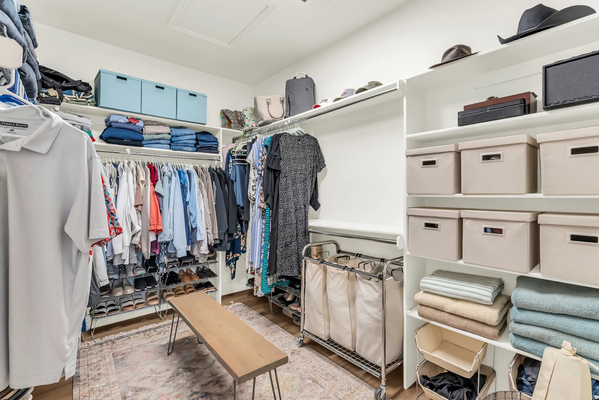 Expansive walk-in closet featuring white built-in shelving, multiple hanging rods, and wood-finish flooring