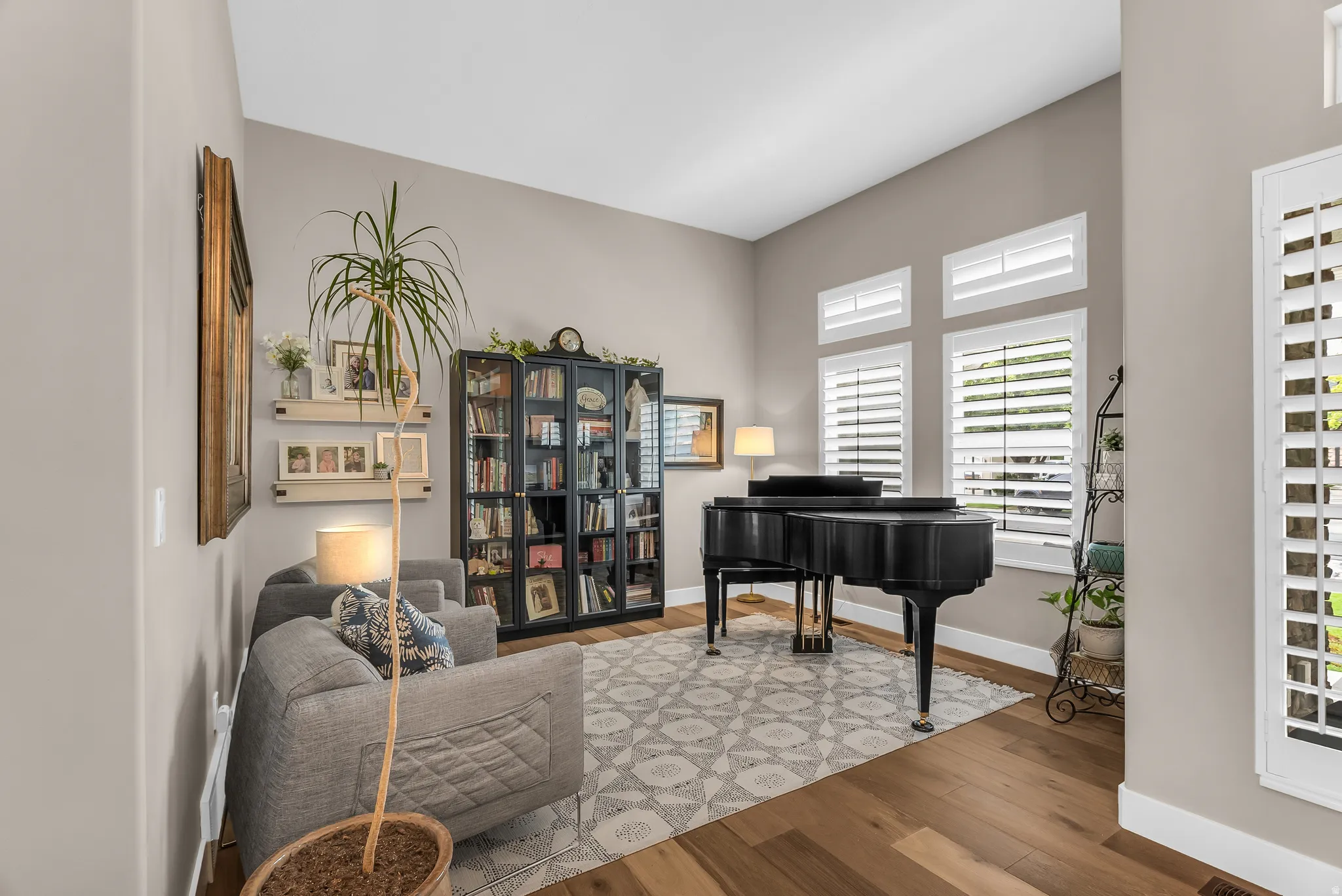 Vaulted ceiling, wood-finish flooring, multiple windows with white shutters, built-in shelving, and a glass-front display cabinet