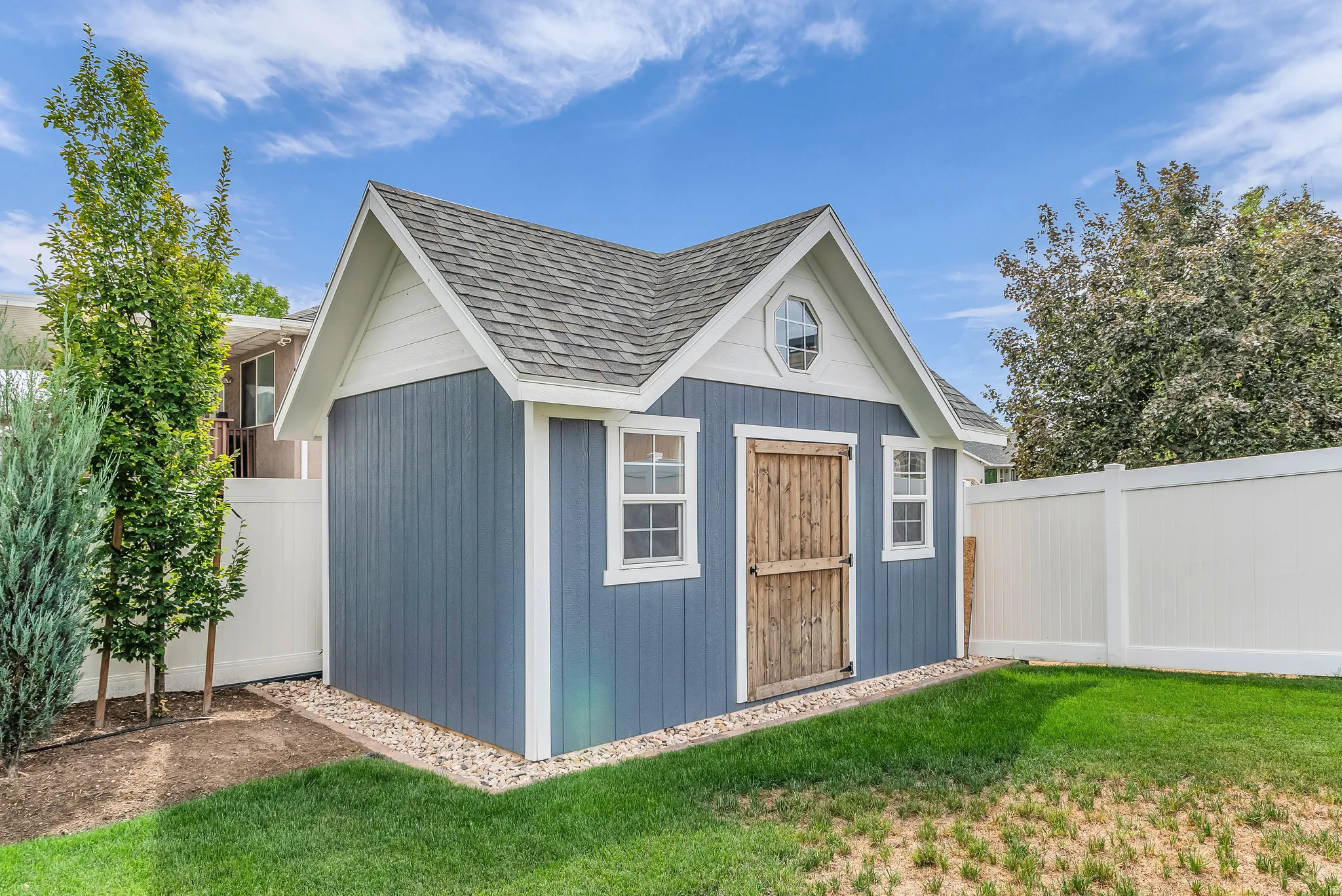 Blue-sided storage shed with a shingled roof, white trim, and a wood-panel door