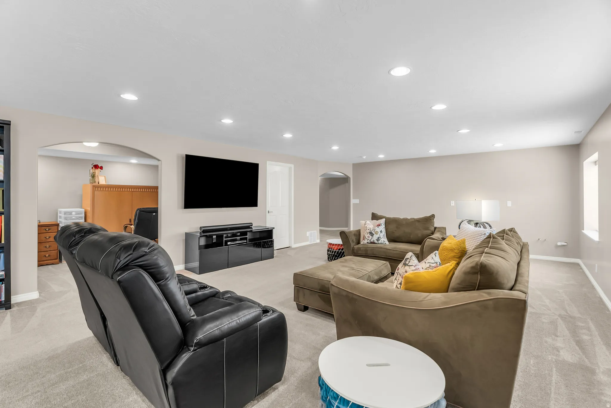 Recessed ceiling lighting, light gray wall paint, light gray carpet flooring, arched doorway, and built-in media console