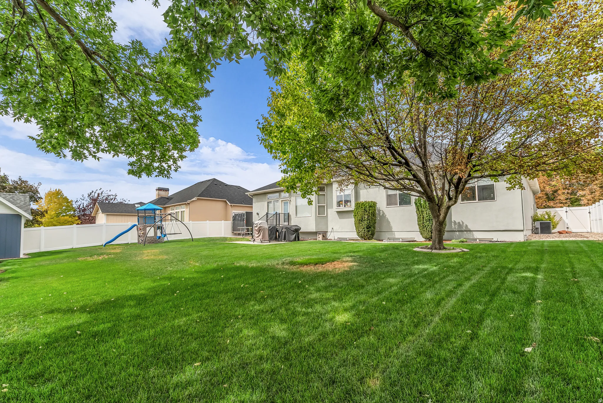 Expansive backyard featuring a manicured lawn, mature trees, and a white privacy fence