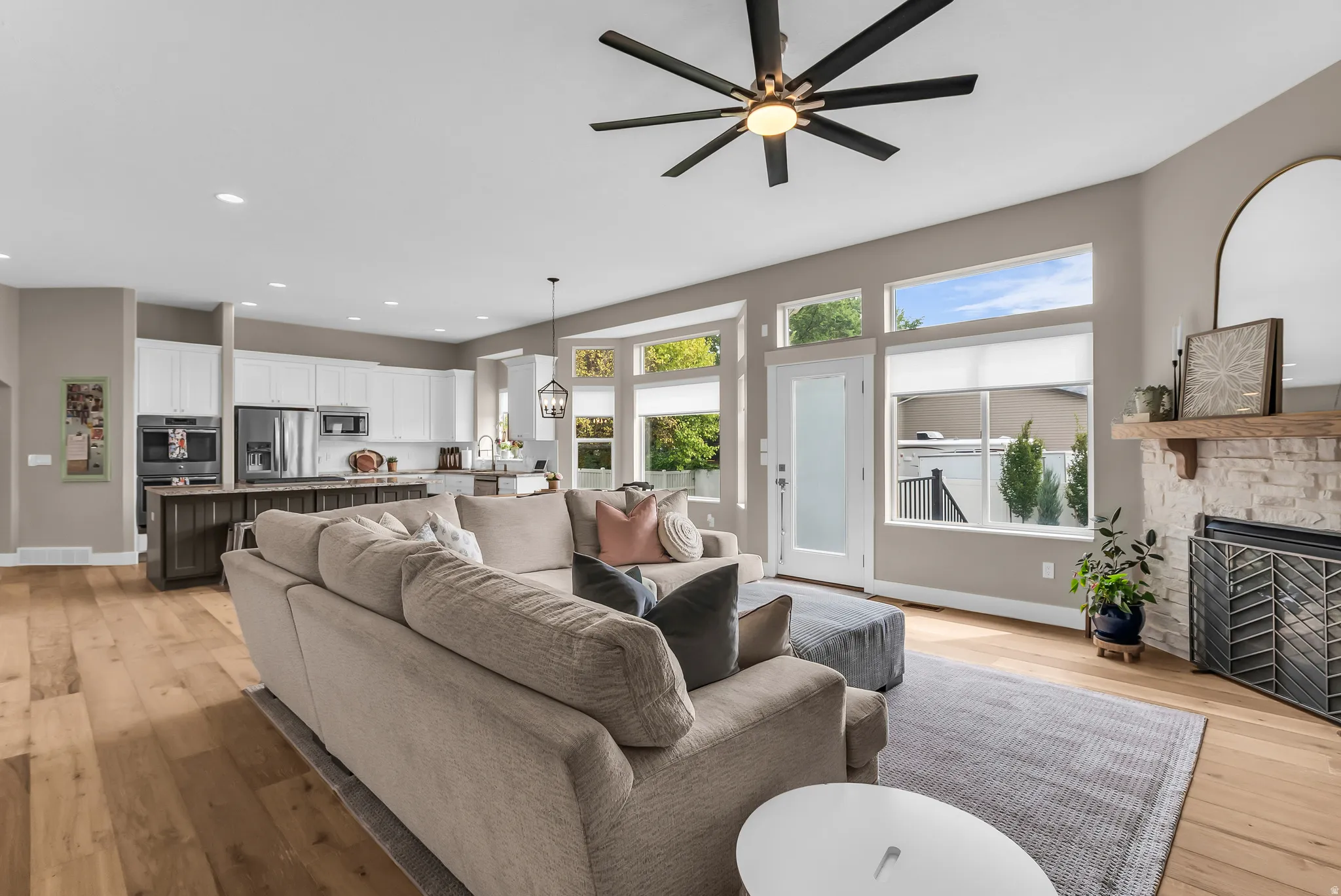 Open-concept living area featuring wood-finish flooring, a stone-faced fireplace, and a contemporary ceiling fan