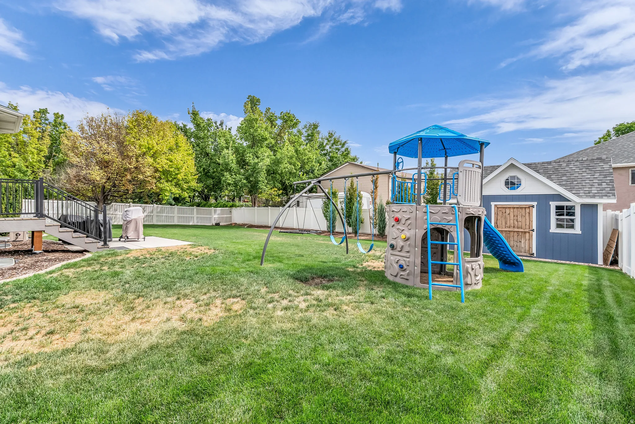 Expansive fenced backyard featuring a wood deck, concrete patio, and mature trees