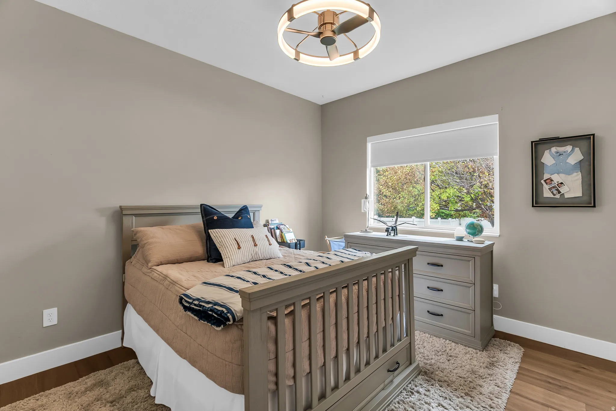 Recessed window with roller shade, wood-finish flooring, and a contemporary ceiling fan with integrated lighting