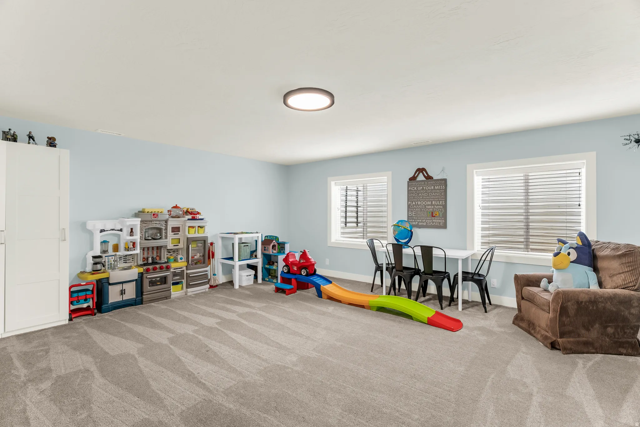 Spacious room with light-colored walls, recessed lighting, two windows with blinds, and light-colored carpeting