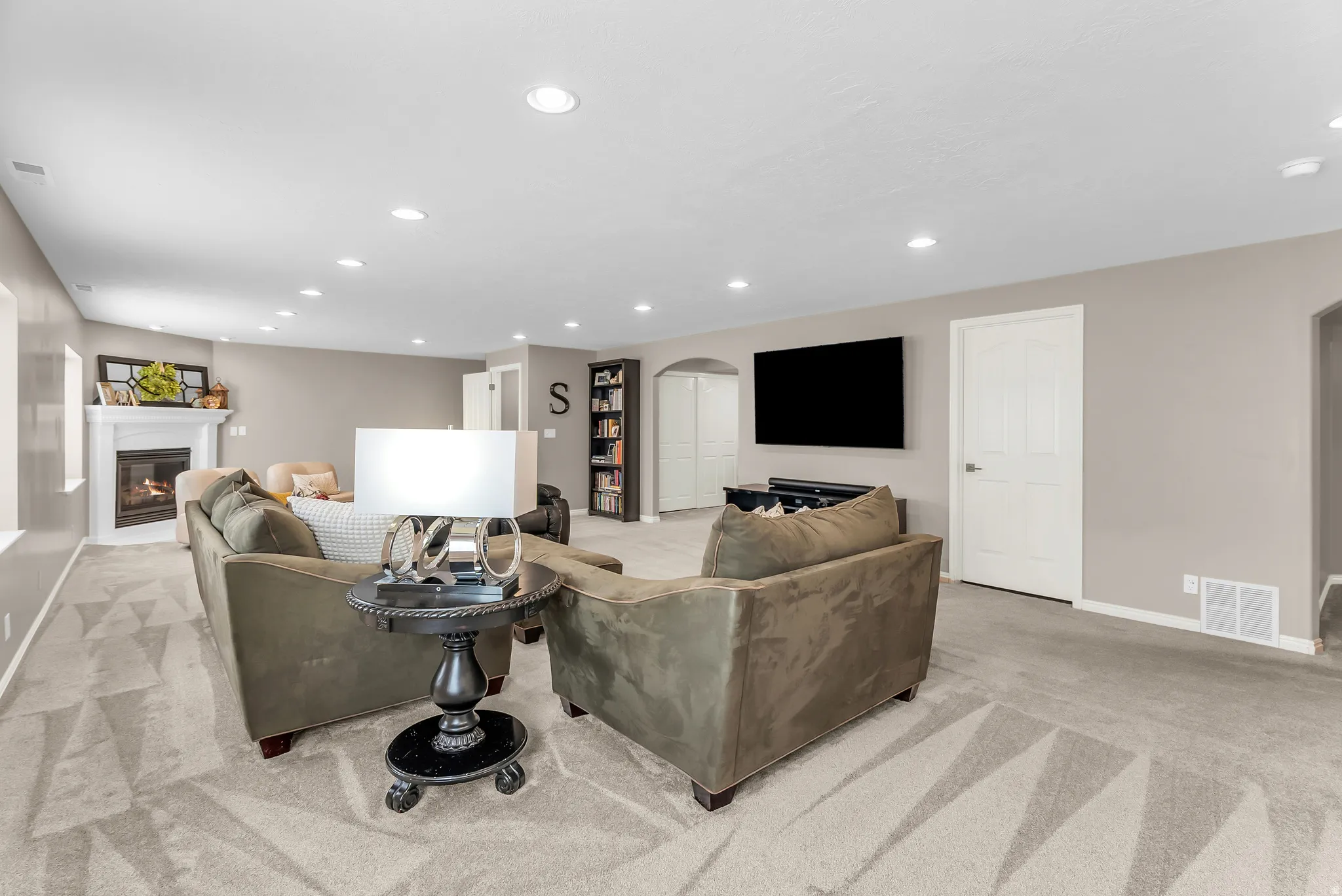 Recessed lighting illuminates a carpeted living area with a white fireplace surround, featuring a hearth and mantel