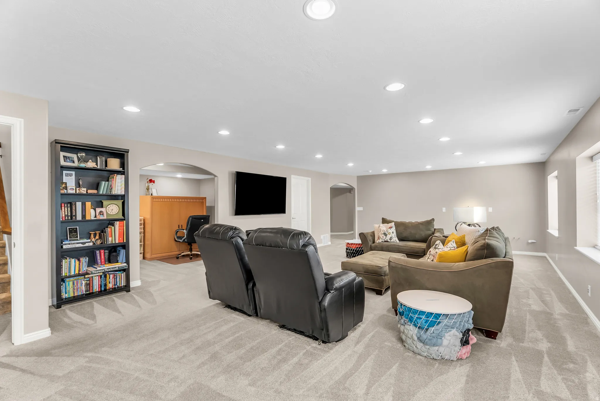 Recessed lighting throughout, arched entryway, built-in shelving, light-toned carpeting, and light-toned wall paint