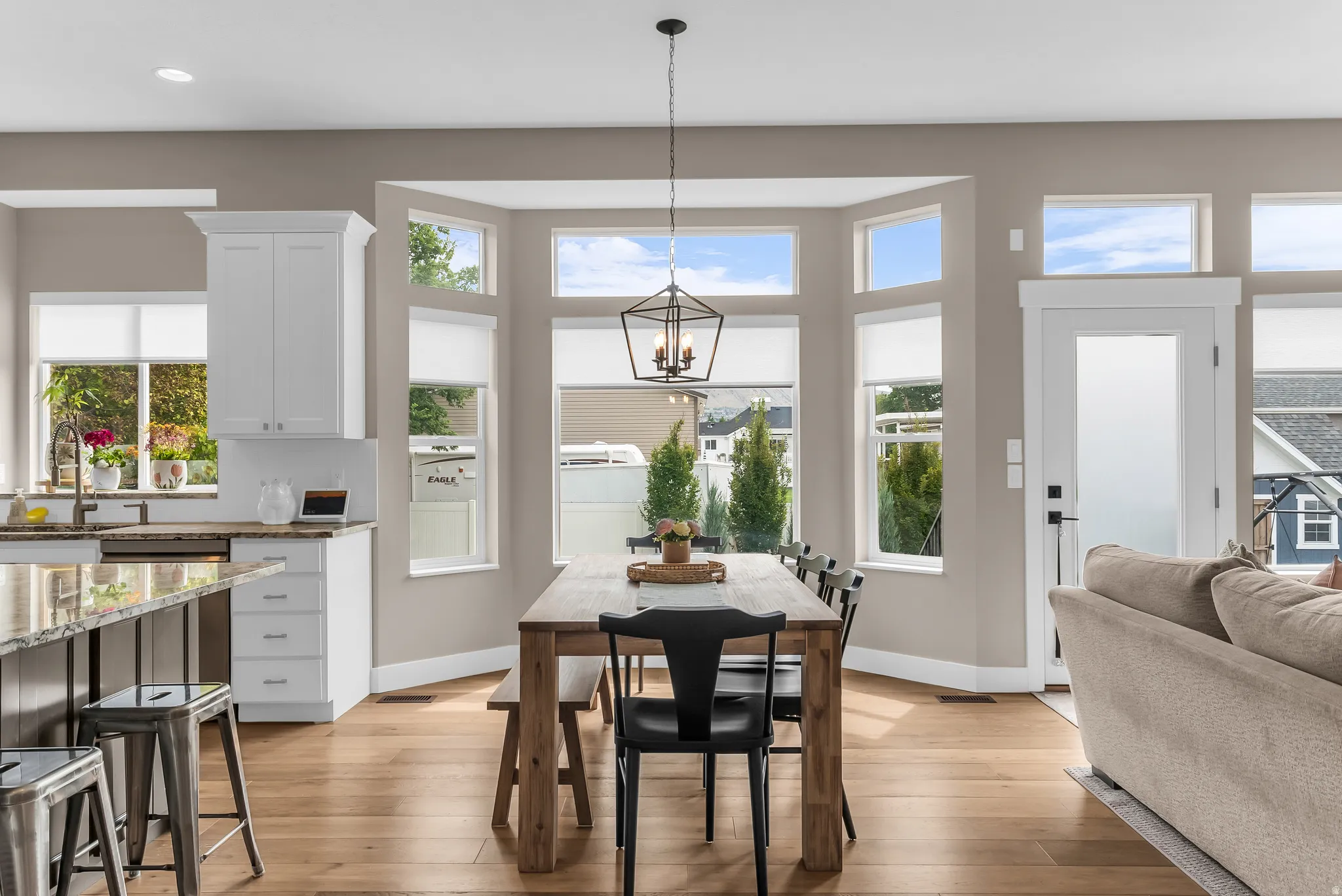 Wood-finish flooring throughout, bay windows with upper transom windows, white kitchen cabinetry with granite countertops, kitchen island with seating, and a modern geometric chandelier