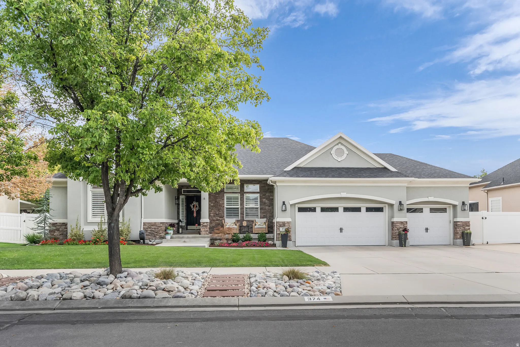 Stucco exterior with stone accents, mature landscaping, two-car garage, and an additional single-car garage