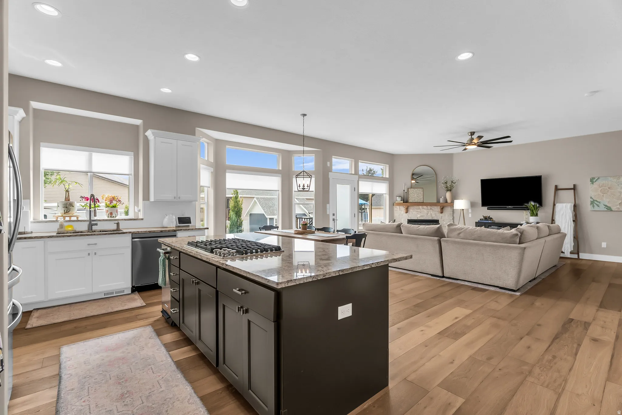 Open-concept design featuring wood-finish flooring, a kitchen island with cooktop, white perimeter cabinetry, granite countertops, and a living area with a fireplace