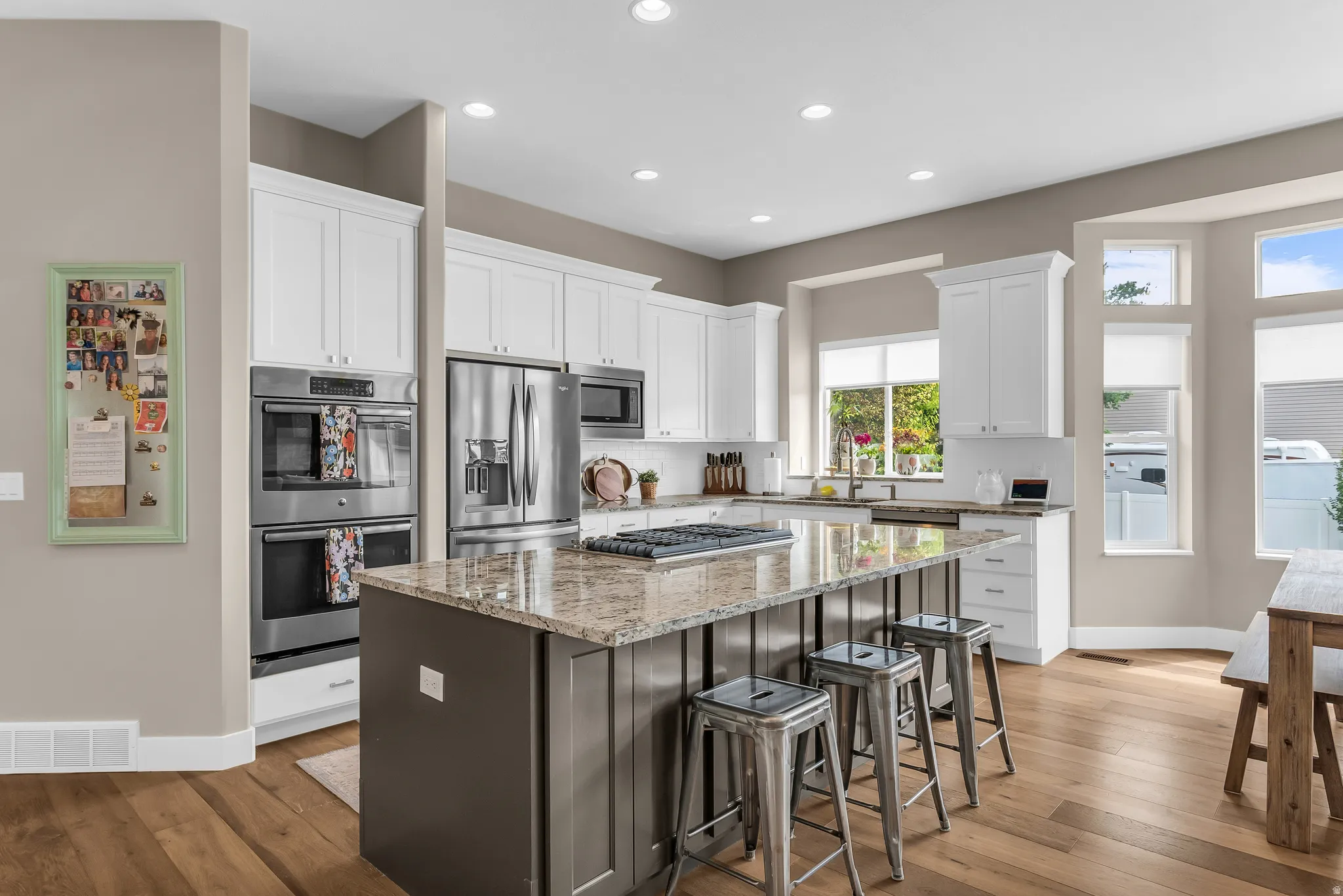 Kitchen featuring wood-finish flooring, white cabinetry, a central island with a stone countertop, stainless steel appliances, and recessed lighting