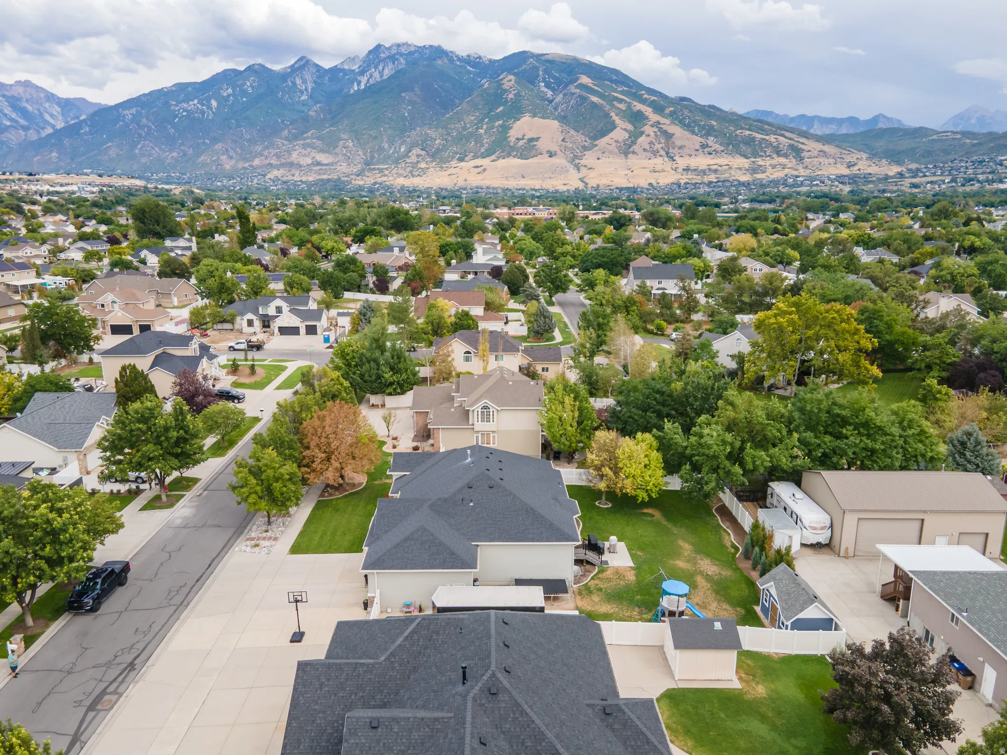 Residential neighborhood with mature trees, mountain backdrop, paved streets, and a variety of home styles