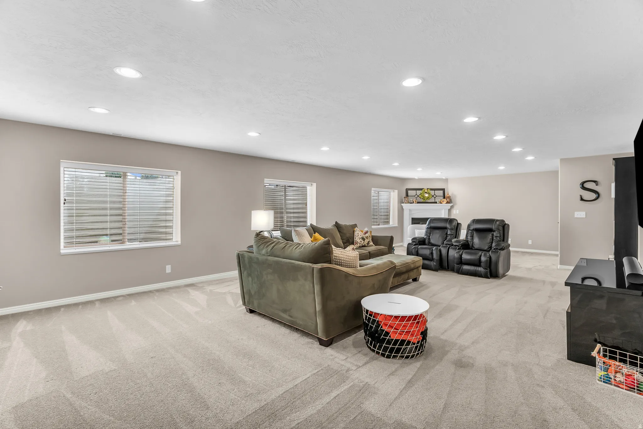 Expansive open-concept room featuring recessed lighting, light-toned carpeting, multiple windows, and a built-in fireplace with a white mantel
