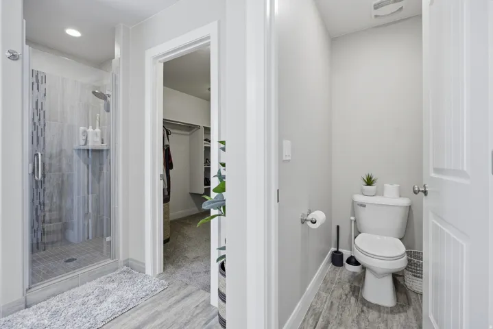 Master bathroom. Glass-enclosed shower with tile surround and integrated shelving, wood-finish flooring, and a separate water closet