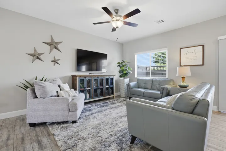 Wood-finish flooring with light gray walls, a ceiling fan, and a entertainment console