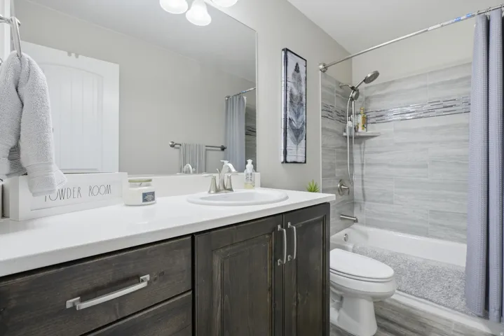 Guest Bathroom featuring a dark wood-finish vanity with a white countertop and undermount sink, a large wall-mounted mirror, and a tub with surround and decorative accent band