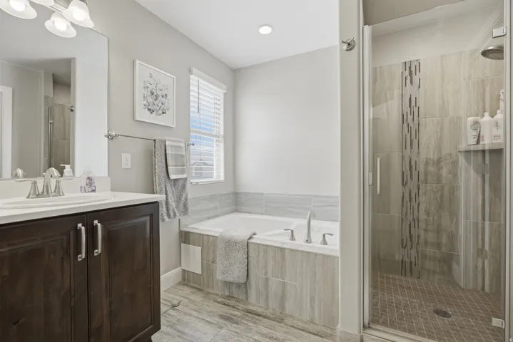 Master bathroom. Built-in soaking tub, separate glass-enclosed shower, wood-finish flooring, dark wood vanity, and a window with blinds