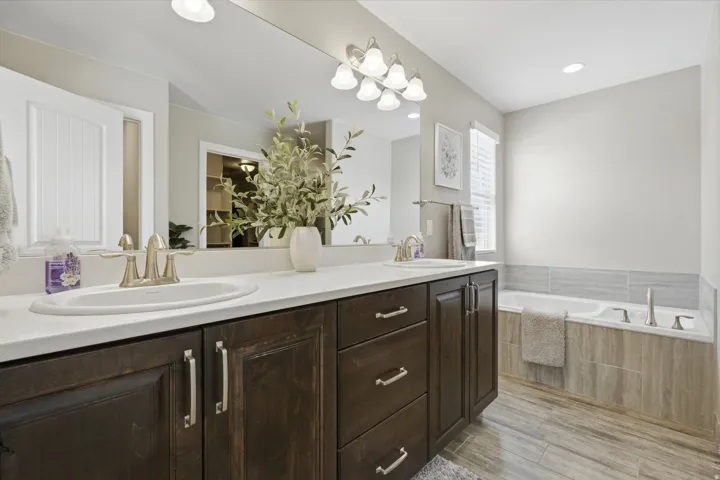 Master bathroom, Dual vanity with integrated sinks, dark wood-finish cabinetry, built-in soaking tub, wood-finish flooring, and wall-mounted light fixture