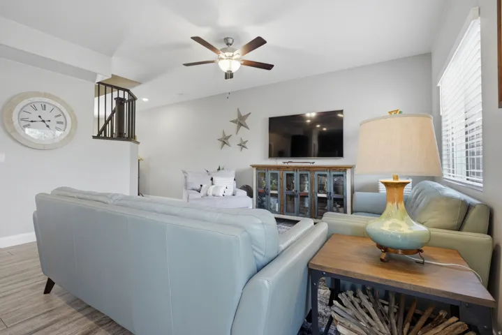 Wood-finish flooring, ceiling fan with integrated lighting, window with blinds, and staircase with dark railings