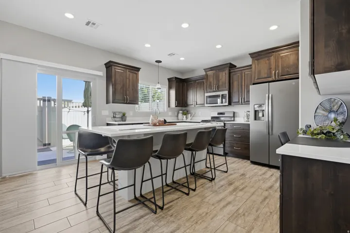 Kitchen featuring dark wood-finish cabinetry, stainless steel appliances, a center island with countertop seating, and wood-finish flooring