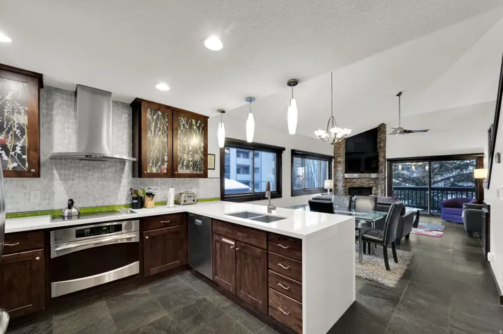 Open-concept living area with vaulted ceilings, a kitchen island, integrated stainless steel appliances, and a stone-clad fireplace