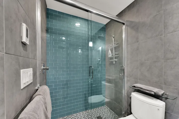 Glass-enclosed shower with blue subway tile surround and pebble tile flooring