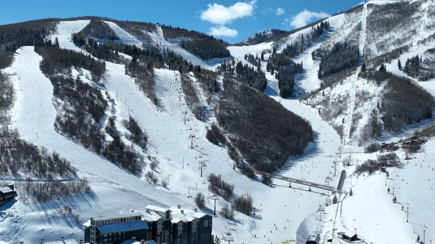 Snow-covered mountainside with multiple ski slopes, visible ski lifts, and a building with a dark-toned facade
