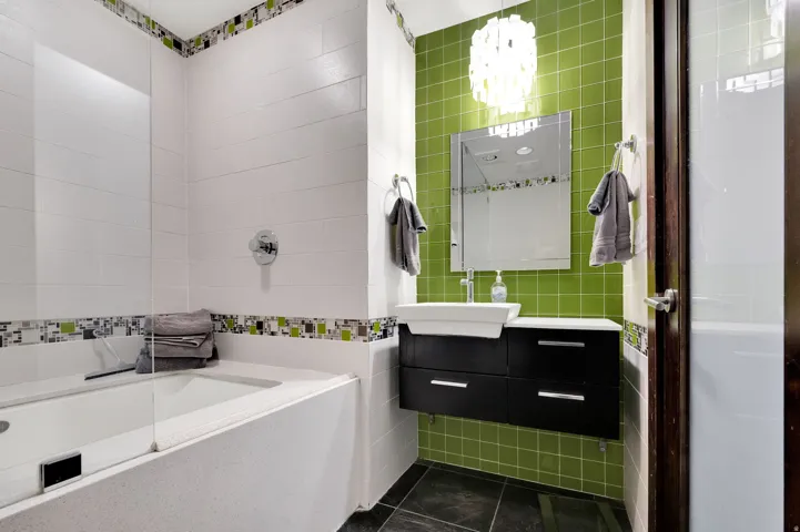 Built-in bathtub with glass partition, white tile surround, mosaic accent tile, floating vanity with vessel sink, and textured green wall tile