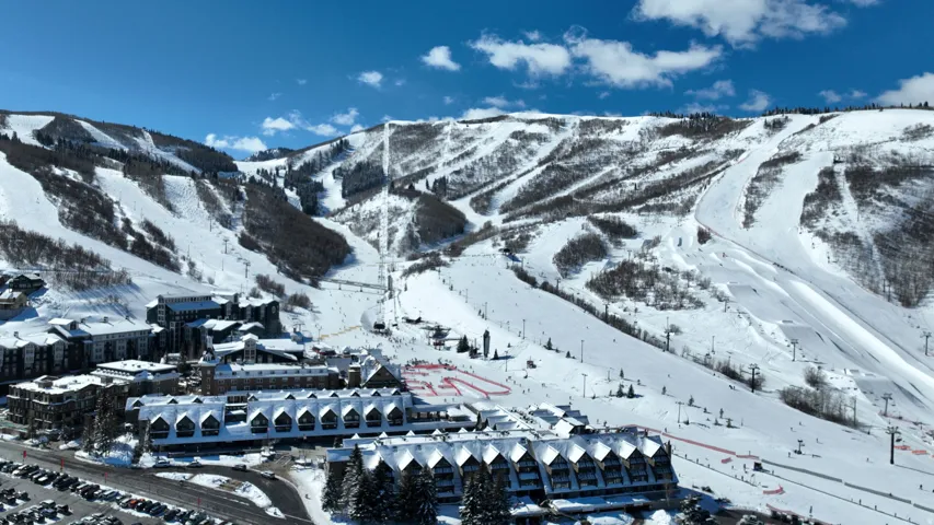 Expansive snow-covered mountain terrain, ski slopes, multiple buildings with snow-dusted roofs, and a large parking area