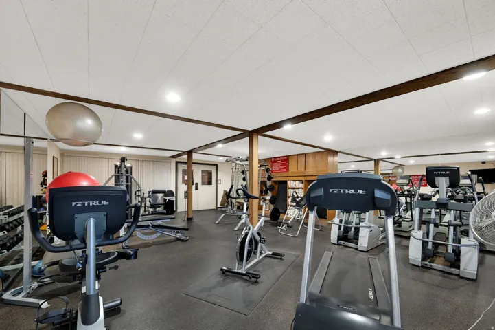 Dedicated fitness area featuring rubber flooring, recessed lighting, and exposed wood beams