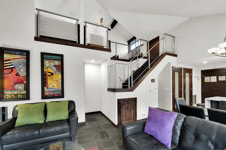 Vaulted ceiling with exposed beams, slate tile flooring, open loft area with cable railing, dark wood-finish staircase, and built-in storage