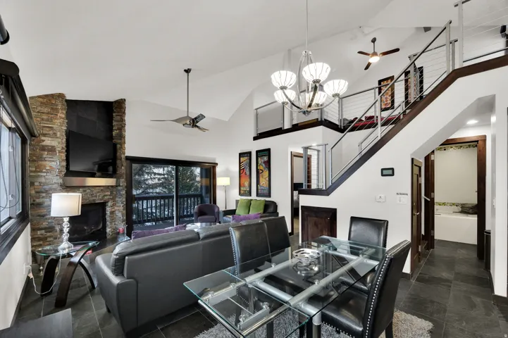 Vaulted ceilings, a stone-clad fireplace, and a sliding glass door leading to an outdoor balcony