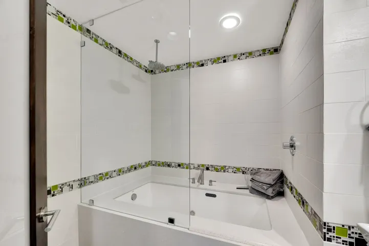 Bathtub with a glass enclosure, white tile surround, and decorative tile accents