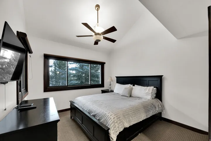 Vaulted ceiling with a ceiling fan light fixture, dark wood window trim, and wall-to-wall carpeting
