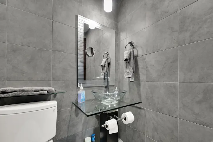 Full-height wall tiling, contemporary vessel sink, glass vanity counter, wall-mounted mirror, and modern toilet
