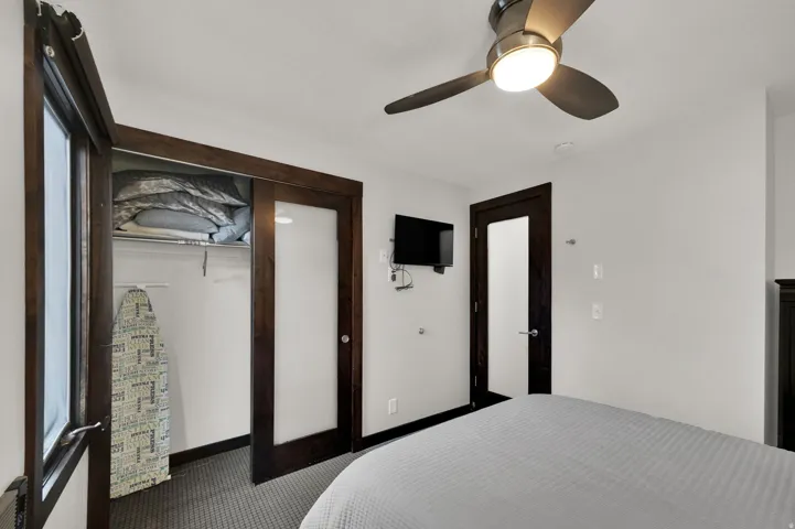 Ceiling fan with integrated lighting, wood-finish doors, glass-paneled closet door, wall-mounted television, and light gray wall paint