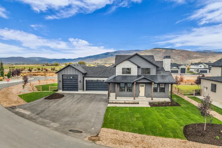 Modern farmhouse exterior featuring stone accents, a metal roof, a covered porch with timber posts, and an attached three-car garage