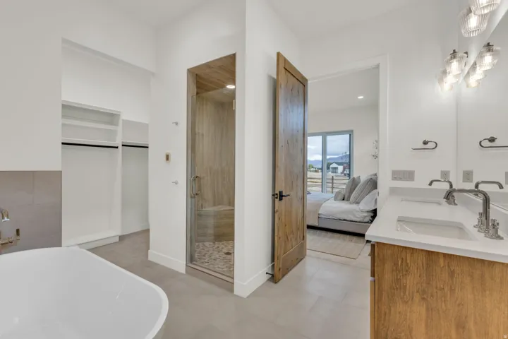 Freestanding soaking tub, wood-finish vanity with dual sinks, tiled shower with glass enclosure, built-in closet shelving, and a solid wood door